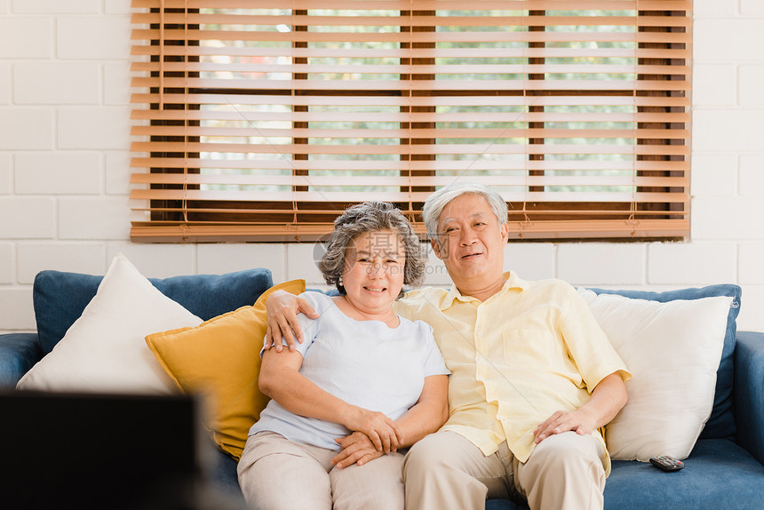 在家里客厅看电视的年长夫妇甜蜜的享受爱时刻同躺在沙发上家里放松享受老年庭的时尚生活方式图片
