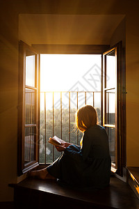 女孩坐在窗边的地板上阅读一本书背景图片