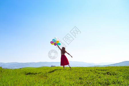 锡耶纳红色在草地上快乐的女孩带着多彩的气球在蓝天和绿草地上背景