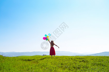 锡耶纳红色在草地上快乐的女孩带着多彩的气球在蓝天和绿草地上背景