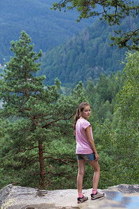 女孩站在岩石悬崖边看着森林山图片