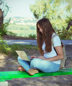 在公园的长椅上坐着笔记本电脑的少女图片