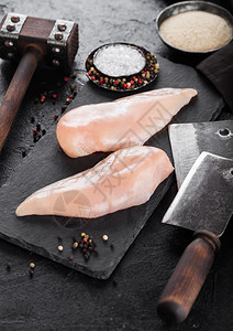 斧头镊子锤子黑石板上的鲜有机鸡片胸黑石板上有肉片和锤子黑上还有香料和草药背景