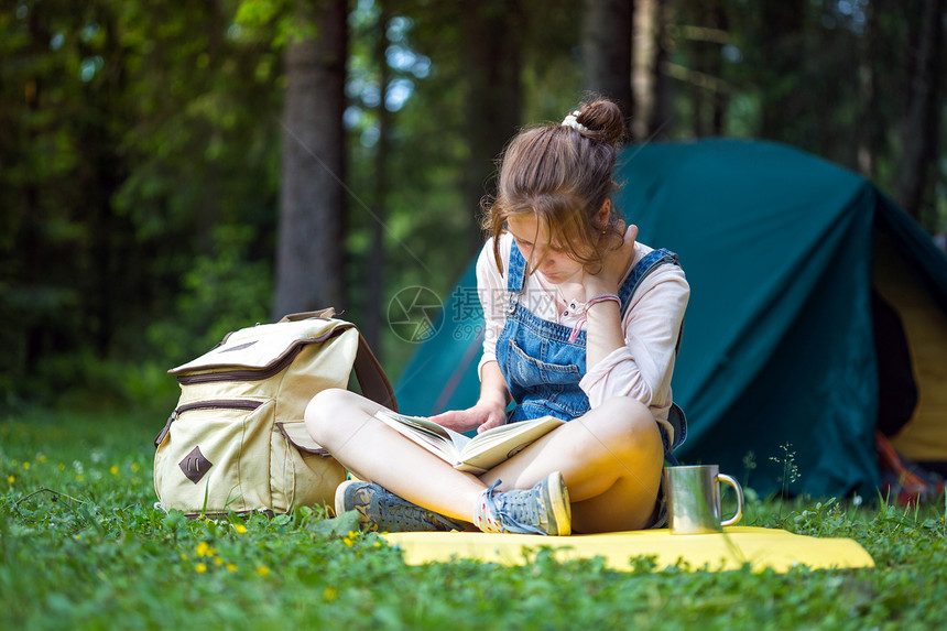 徒步旅行的青年女孩在帐篷附近看书图片