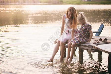 快乐的家庭微笑的母亲和女儿坐在码头上温暖的秋天女性的高清图片素材