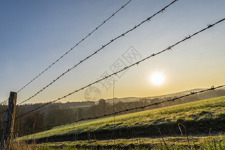 在日出时明亮的春天从德国牧场和绿草地上围起铁丝网栅栏图片