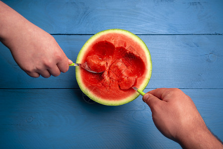 一个女人和男用勺子吃一条西瓜切成两半蓝底直接在美味的夏季水果上方图片