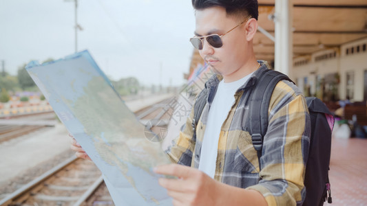 在火车站渡假和等候火车时年轻男旅游随身携带者享受旅行图片