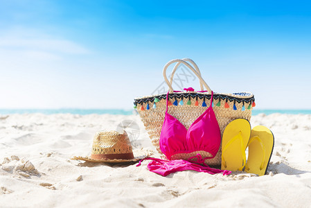 夏季袋拖鞋帽子和比基尼在热带海滩上蓝色的天空背景图片