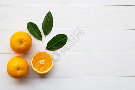 白木本底的橙色柑橘水果和绿叶图片