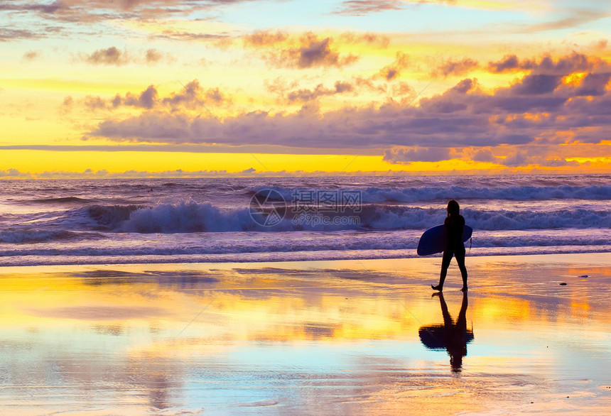 日落时冲浪者带着板在海滩上行走图片