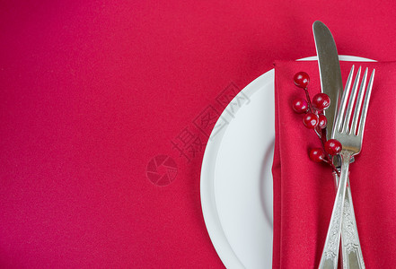 银匙和叉子白瓷板上有刀和叉子红色纸巾薄和胡椒浆白瓷板位于一张上面有红色桌布的子上有文字空间背景