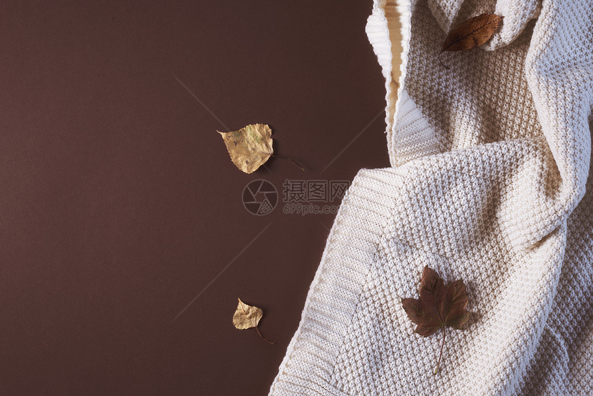 秋天的舒适概念是白毛毯和棕色纸背景上多彩的落叶图片
