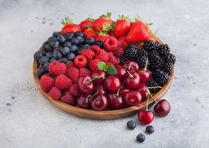 以圆木盘制成的新鲜有机夏季果子混合物放在浅厨房桌底的草莓蓝黑和樱桃图片