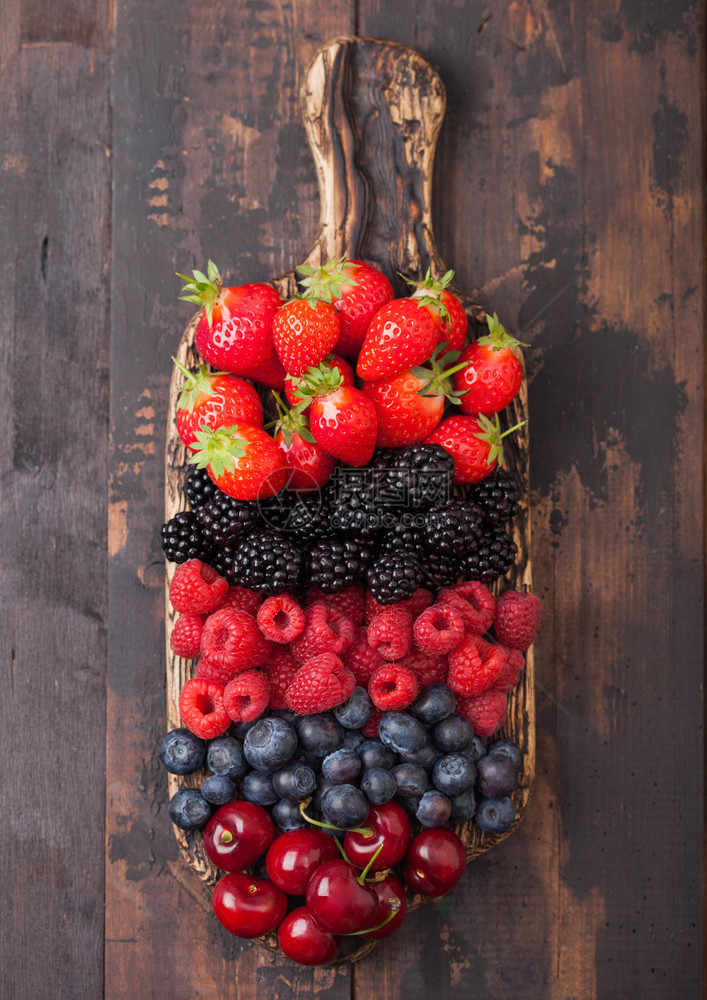 深黑木桌底的旧制切削板上的新有机夏季果子混合物草莓蓝黑和樱桃图片