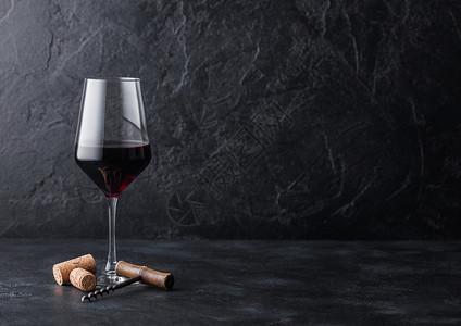 一杯优雅的红葡萄酒配有软木瓶和黑石底的软木瓶背景图片