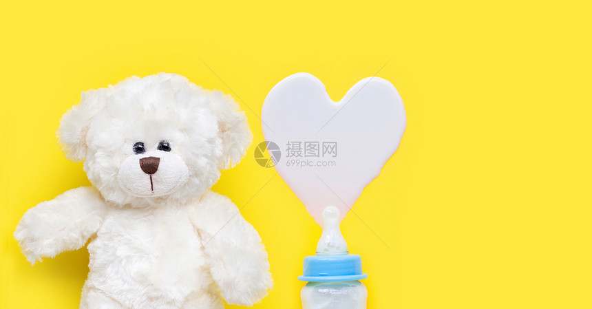黄色背景上的玩具白熊和婴儿奶瓶图片