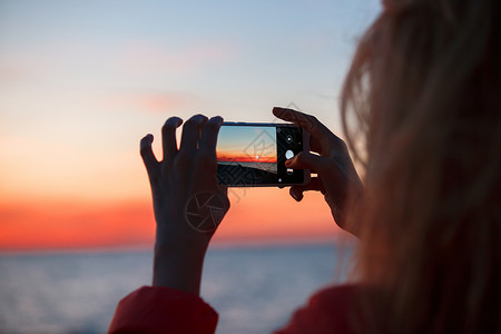 科斯莫女旅行者使用智能手机拍摄多彩的海日落照片女旅行者使用智能手机拍摄多彩的海日落照片背景