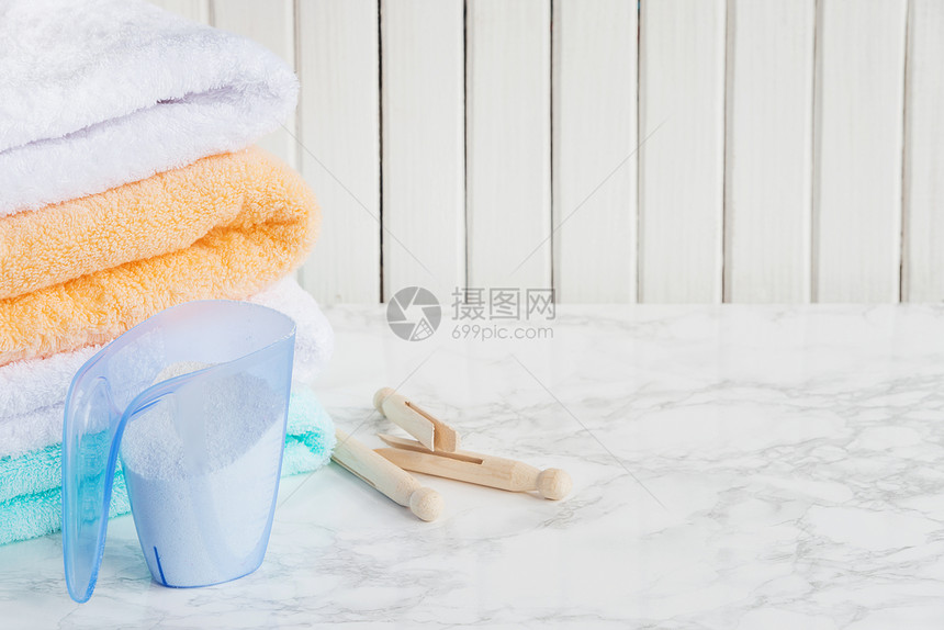 用洗涤剂一堆白色毛巾和木制在大理石表面木制板的白色底面用灰的洗涤剂一叠白色毛巾和木制衣服板用蓝色塑胶水杯测量图片