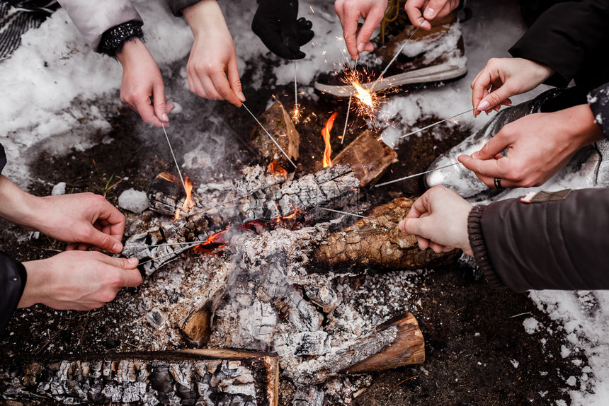 青年在冬季坐森林的营火周围烧着灯光青年在冬季坐林的营火周围烧着灯光图片