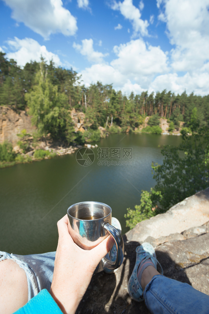 女孩徒步旅行者坐在湖边举杯图片