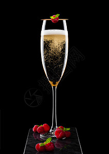 葡萄酒叶高雅的黄色香槟杯子上面有彩虹和新鲜的浆果还有黑大理石板上粘着薄荷叶的背景