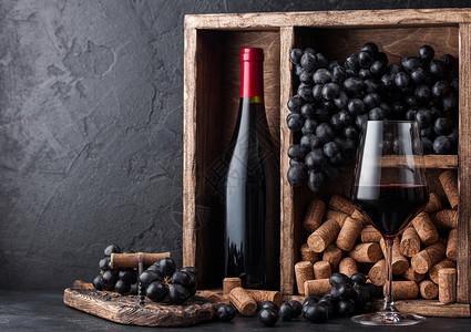 红酒瓶装深葡萄和木箱的软黑石底的旧木箱内装着黑葡萄板上装着软木瓶的优雅葡萄酒杯背景图片