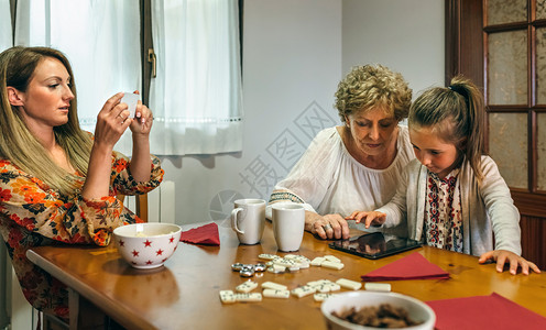 外祖母和孙女在桌子上玩平板小游戏妈妈用手机给她们拍照背景图片