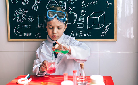 小男孩科学家用化绿色液体从酒瓶里倒在粉笔板上画图片