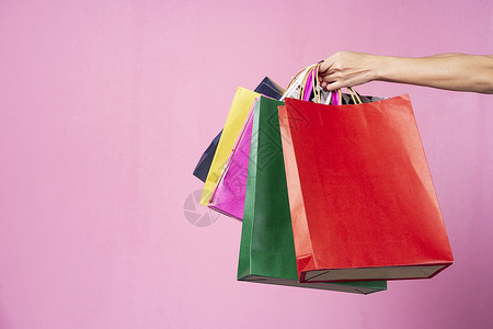 手拿着彩色的购物袋放在粉红背景上空闲间图片