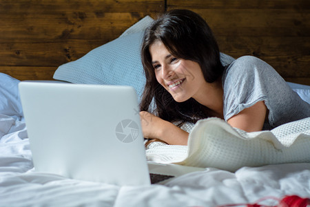 年轻拉丁女在躺家中床上时使用笔记本电脑的肖像漂亮的高清图片素材