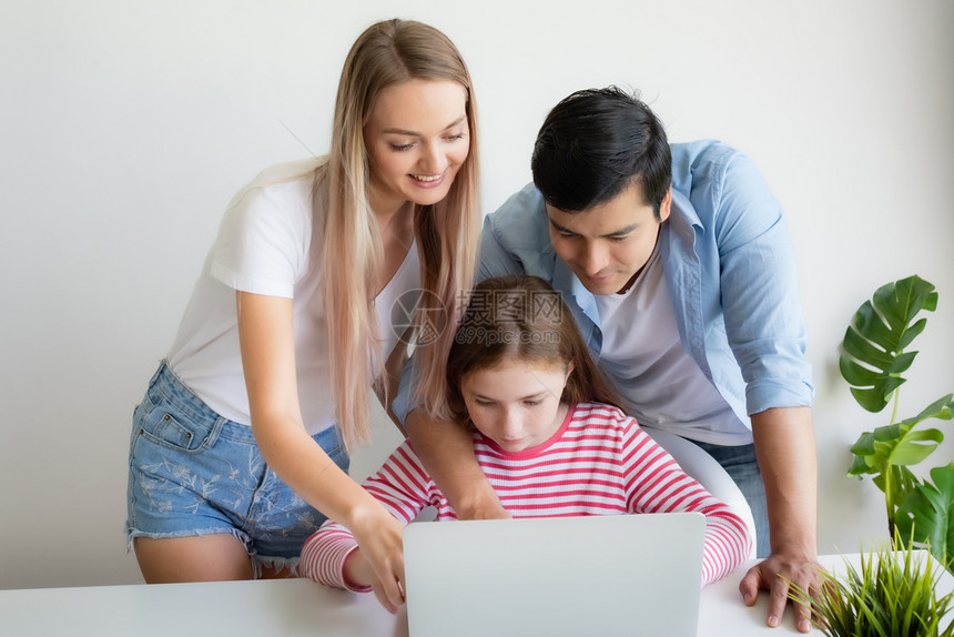 母亲父建议女儿在家使用笔记本电脑在家一起使用年轻家庭概念图片