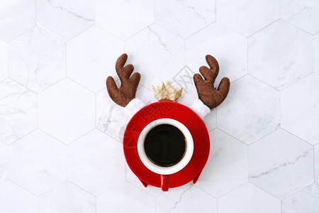 在白大理石背景节日概念的圣诞庆祝活动上用黑咖啡红杯和驯鹿头带举行圣诞节庆祝活动背景图片