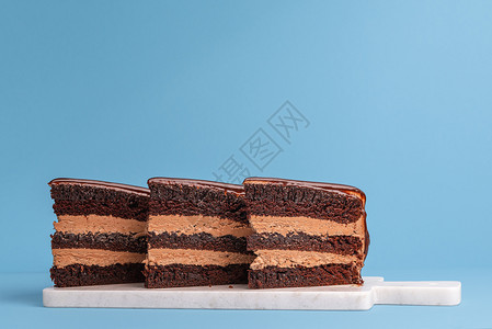 巧克力层蛋糕切片对齐并展示在白切板和蓝背景上生日蛋糕片三部分节日蛋糕图片