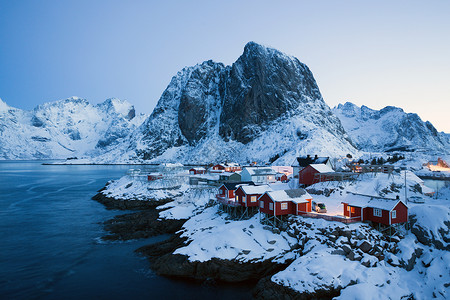 传统的挪威红木屋站在峡湾的岸边和远处山上图片