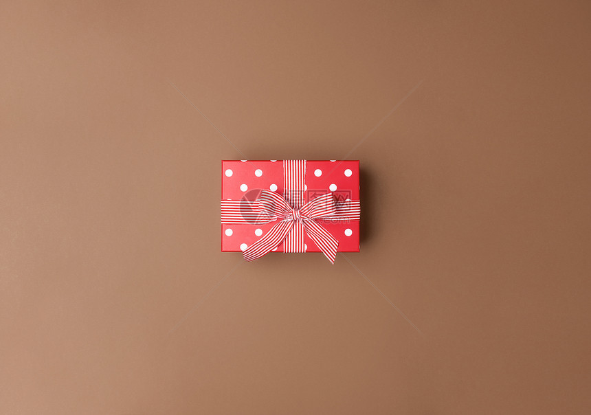 带白点和条纹丝的可爱红色礼物盒棕背景的鞠躬超过圣诞节礼物和弓的视图最小生日礼物图片