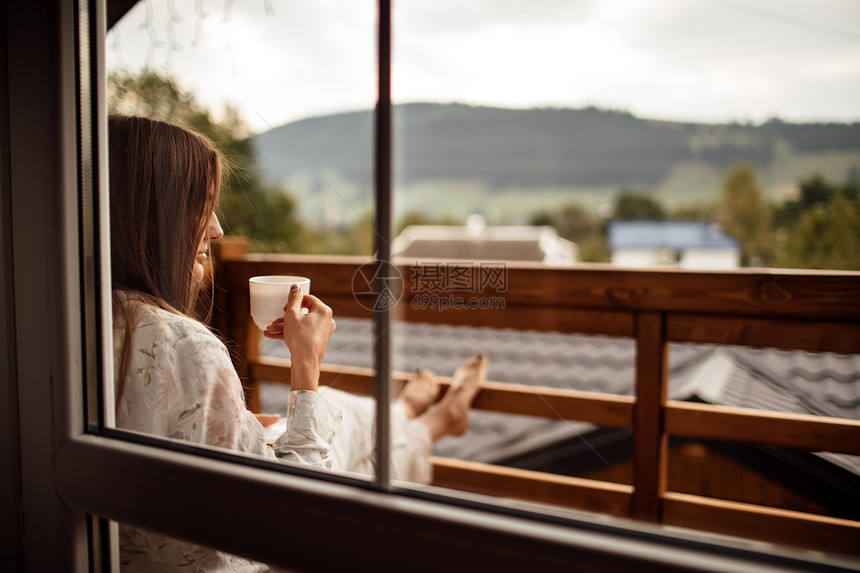 女人早上拿着茶或咖啡看窗边的山图片