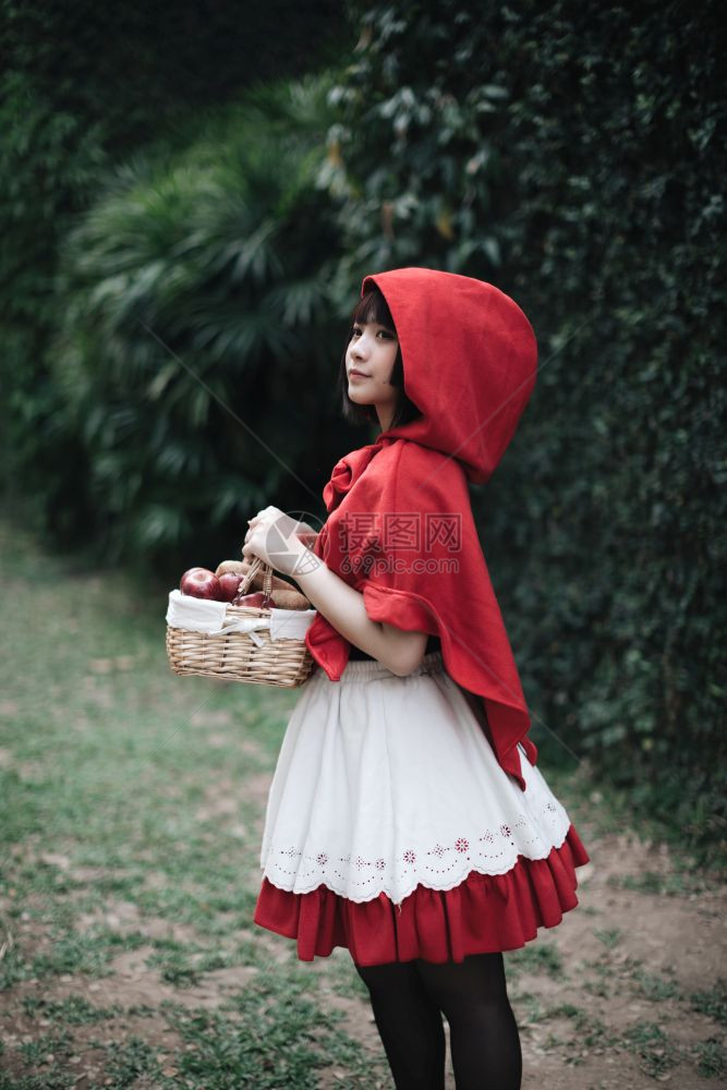 在绿树公园穿着小红色兜帽装饰的年轻女子肖像图片