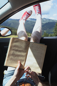 快乐的美丽女孩乘车旅行读山对面的书图片