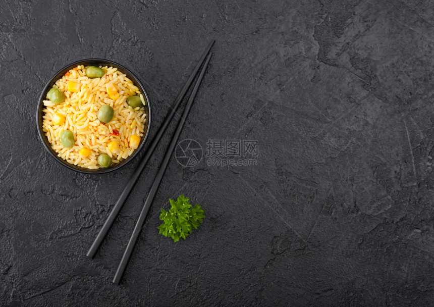 黑碗加煮的有机巴斯马提蔬菜大米黑色的筷子在背景黄的玉米和绿豆子与辣椒片图片