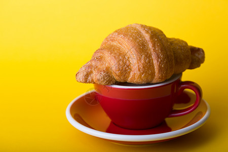 黄底带卡布奇诺和羊角面包的美丽咖啡红杯背景图片