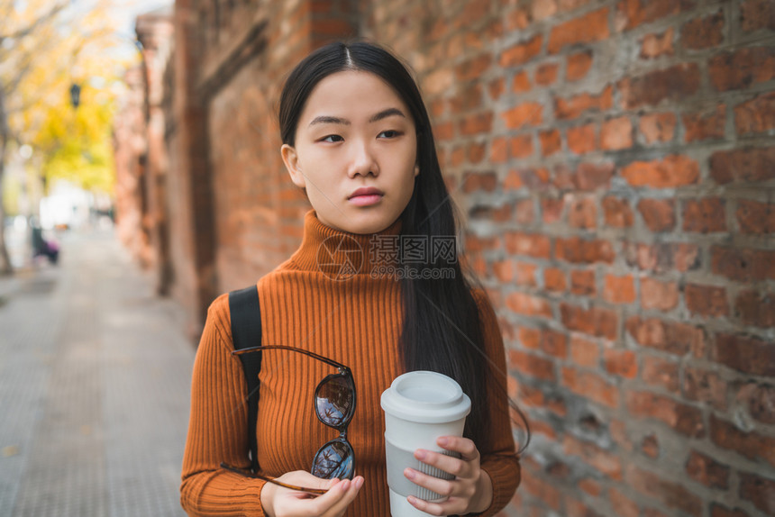 年轻亚洲女在街上露天站着时拿咖啡杯图片