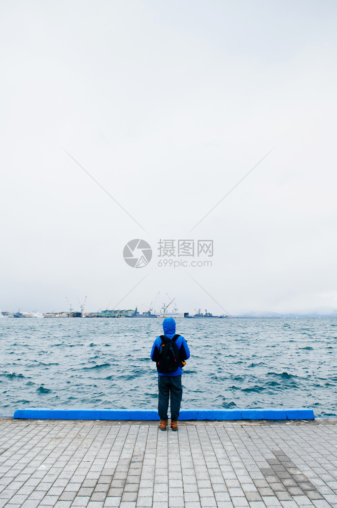 身穿蓝帽衫站在海港边缘图片