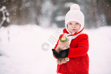 玩雪的小女孩穿着红大衣的小女孩和一只泰迪熊在冬天玩得开心女孩在雪地玩耍女孩在冬天玩得开心背景