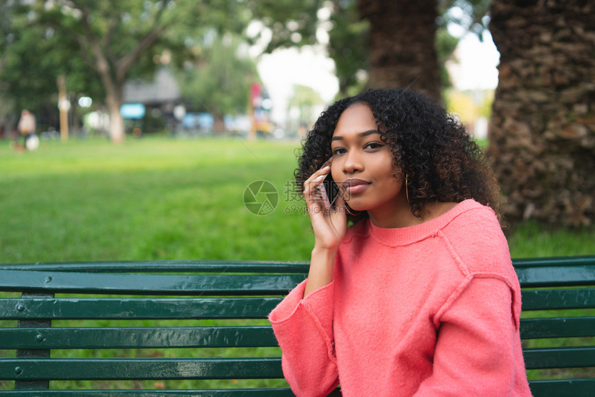 年轻美丽的国女人肖像在电话上交谈坐在公园的长椅上户外图片