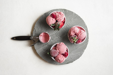 灰色圆盘上碗里自制的草莓冰淇淋上面有浆果冰淇淋和冻水果红色淇淋勺夏季甜点背景图片