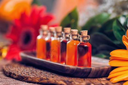 木板上装满红和橙色基本油的透明瓶子红花和油盐灯底芳香疗法放松概念护肤品高清图片素材