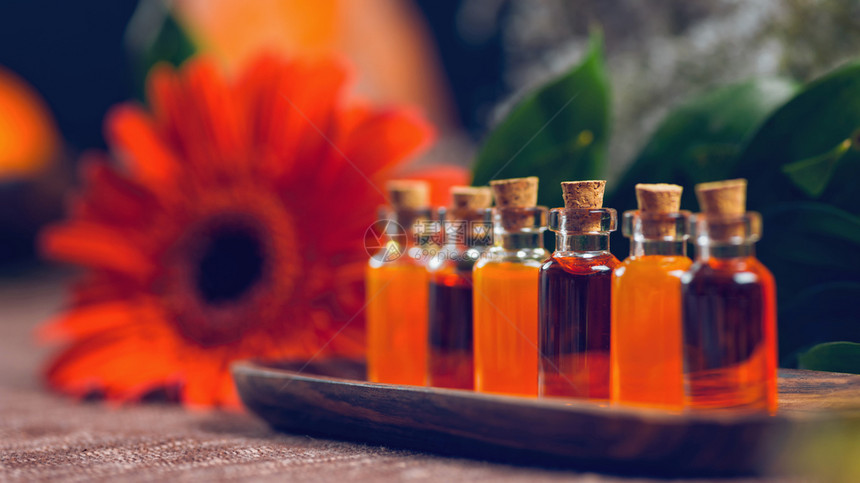 木板上装满红和橙色基本油的透明瓶子红花和油盐灯底芳香疗法放松概念图片