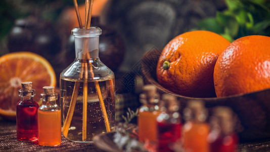 装满红色和橙基本油芳香药瓶的子里面有木棍新鲜柑橘水果橙子和石灰被切成两半绿色植物背景棍枝高清图片素材