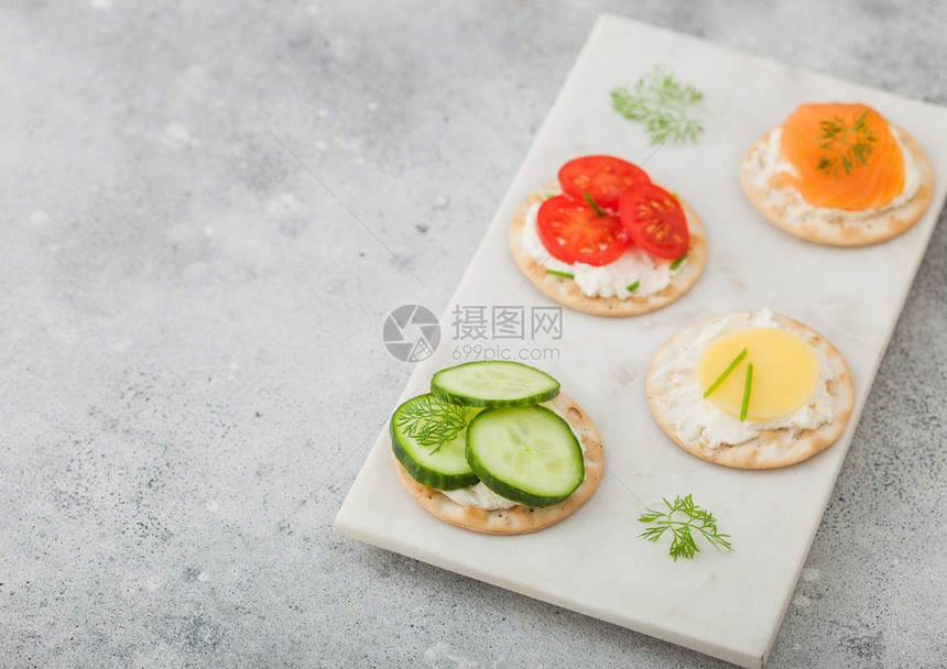 各种圆形健康饼干有鲑鱼和奶酪西红柿黄瓜在光桌背景的大理石板上图片